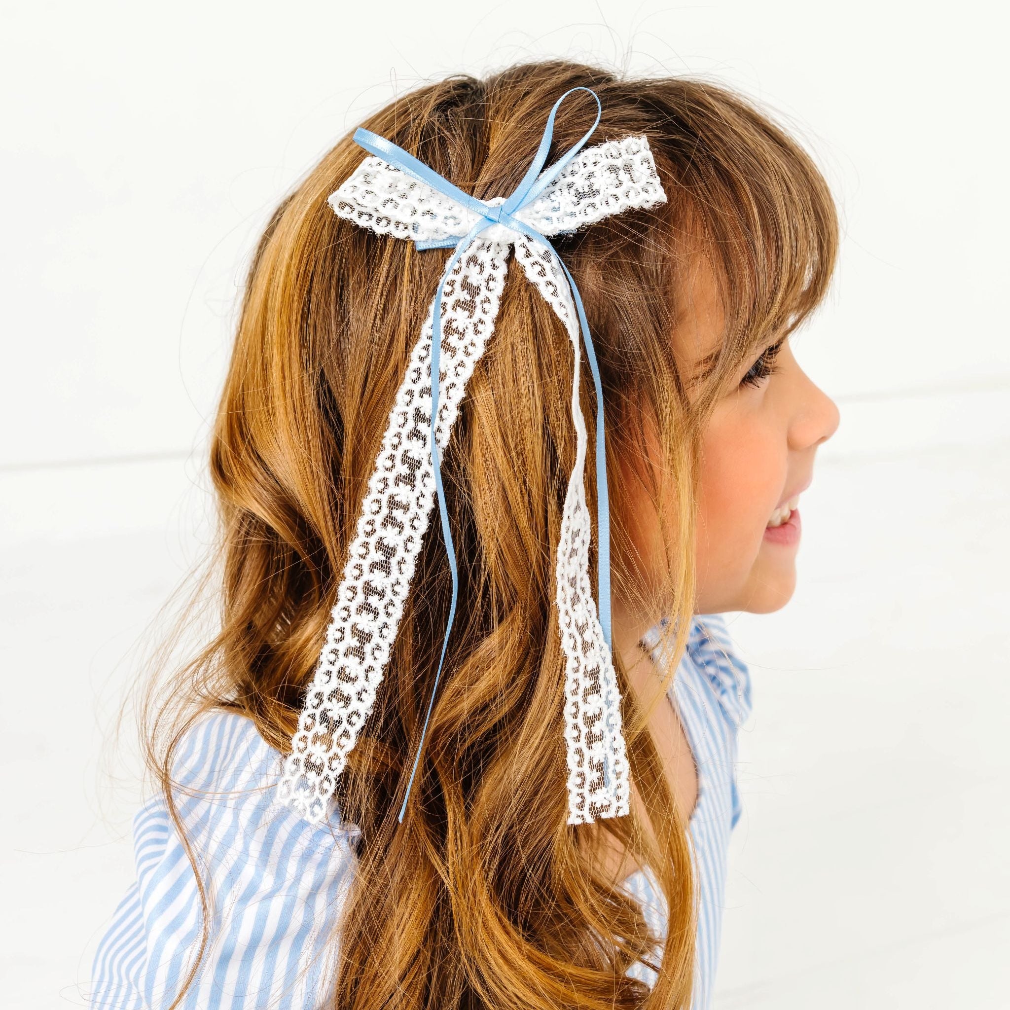 young girl wearing white long tail lace bow with think blue satin ribbon paired with matching blue pinstripe dress for spring