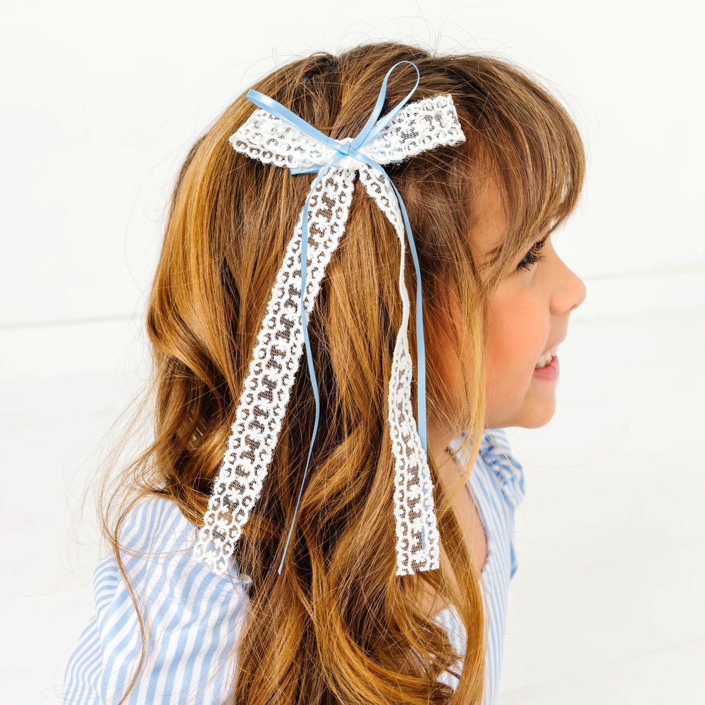 young girl wearing white long tail lace bow with think blue satin ribbon paired with matching blue pinstripe dress for spring