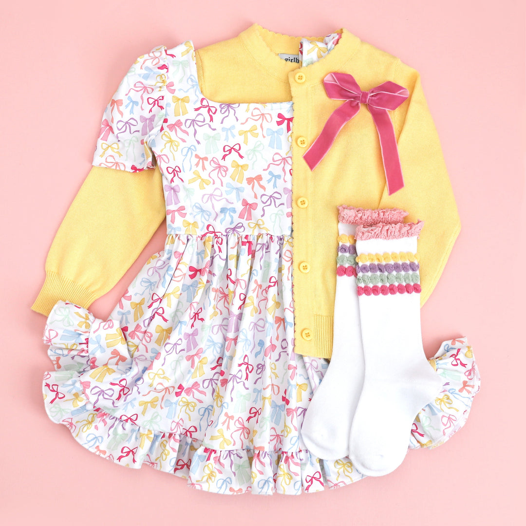 girls spring outfit with square neck white bow print dress, yellow knit cardigan, pastel bubble knee highs and pink velvet bow