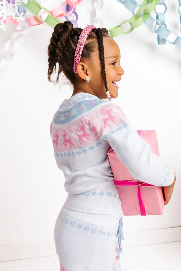 girl holding pink Christmas gift in white sweater and skirt set with pink and blue fair isle print and matching pink sequin headband