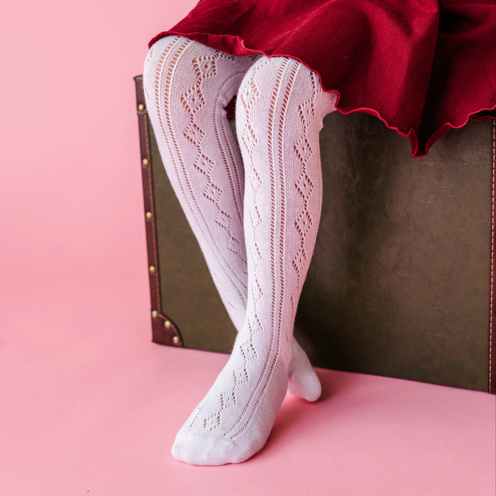 young girl sitting on green suitcase in white open knit tights with burgundy lettuce hem twirl dress for fall