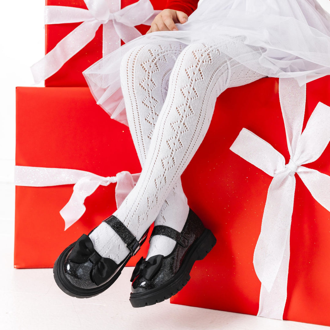 little girl sitting on Christmas gifts wearing white open knit tights with Santa tutu dress