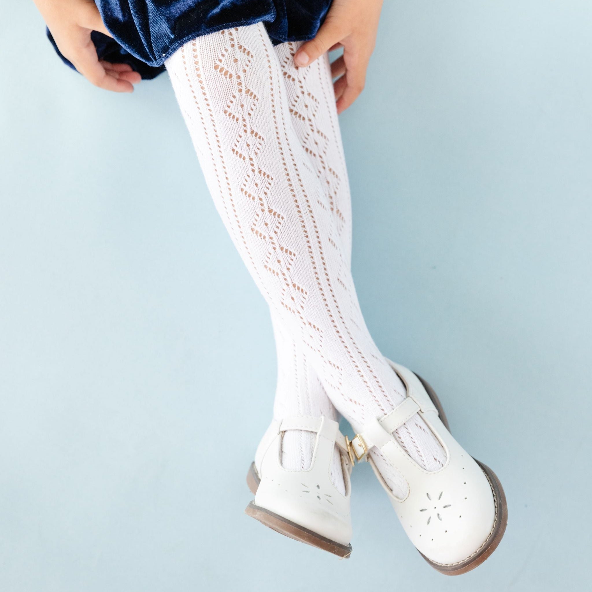 girl sitting in winter white crochet knit tights paired with navy blue velvet twirl and white mary jane shoes