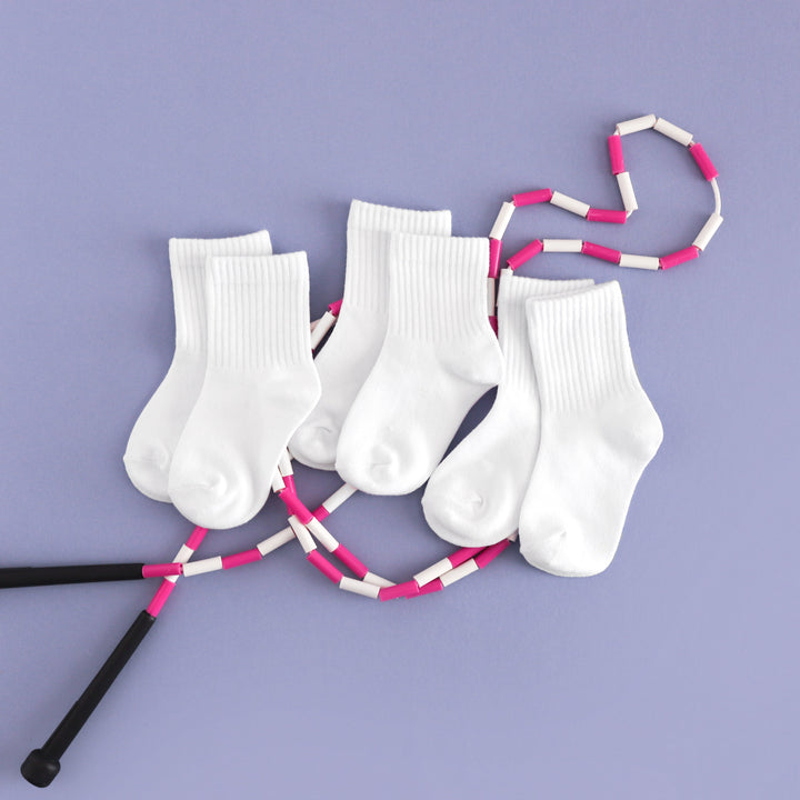 flat lay of children's white crew socks and pink jump rope