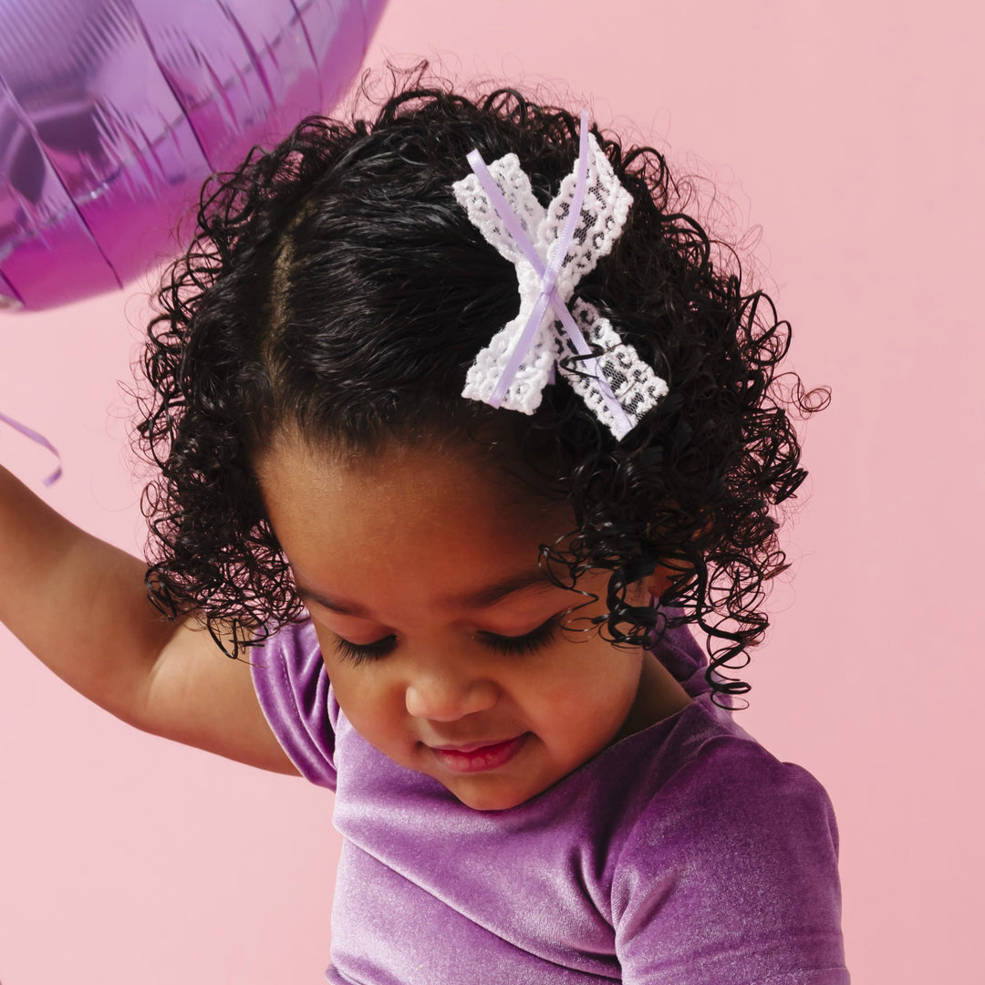 little girl holding purple balloon in lavender velvet top paired with white lace with lavender thin ribbon pigtail bows on clips