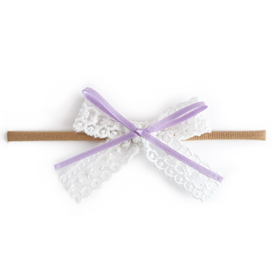 baby girl white lace hair bow with light purple ribbon detail attached to soft stretchy nude nylon headband