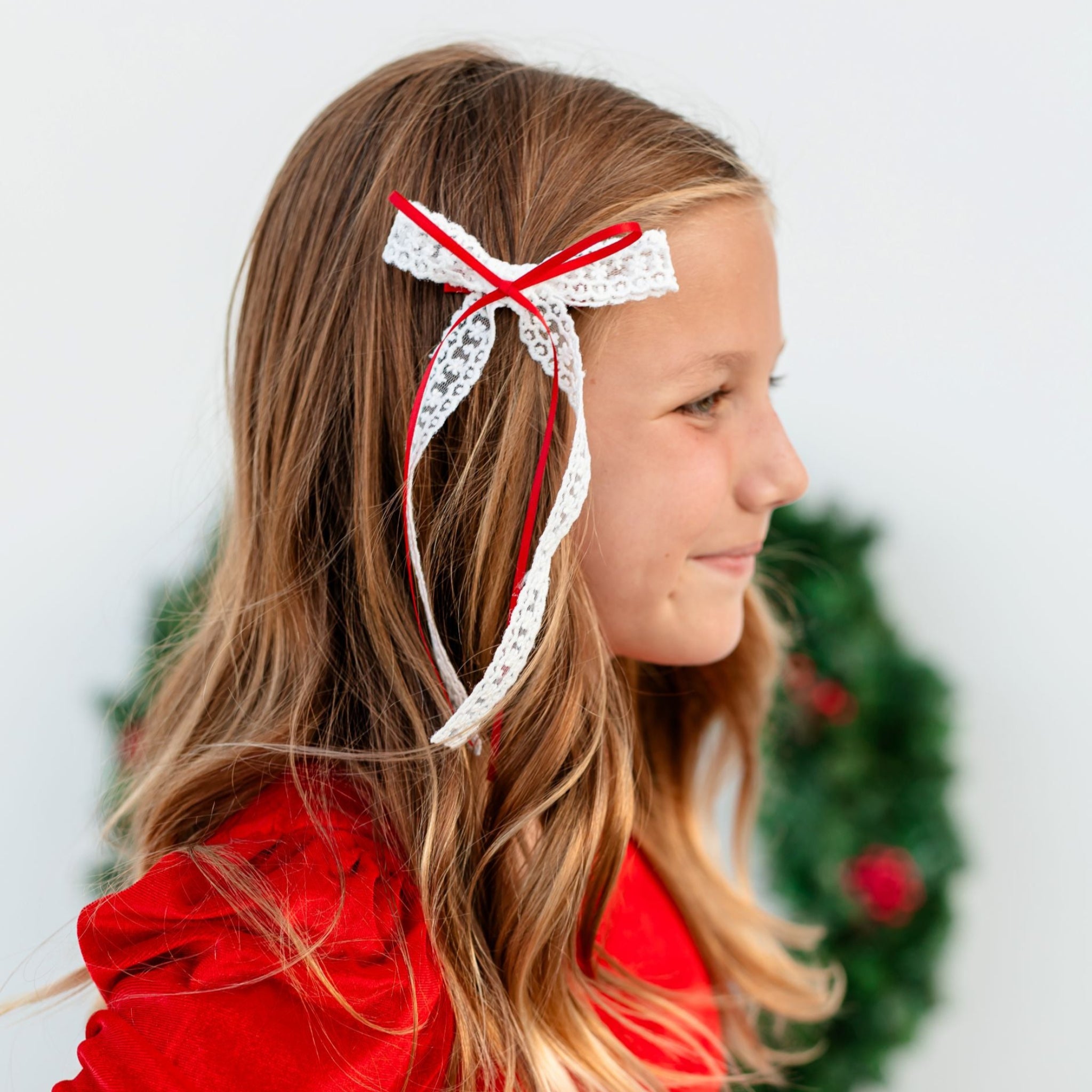 little girl in front of Christmas wreath in white lace bow with red satin ribbon overlay to match Santa baby red velvet  tutu dress