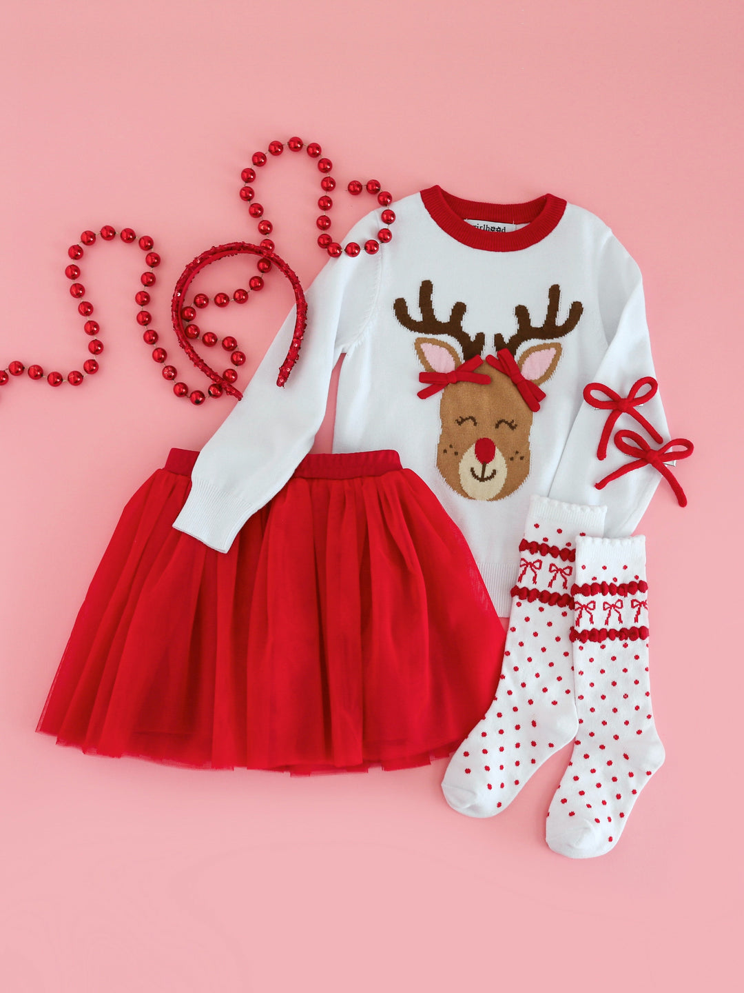 flat lay styled photo of white Rudolph Christmas sweater paired with matching red tulle tutu skirt, red bow socks and red yarn pigtail clips