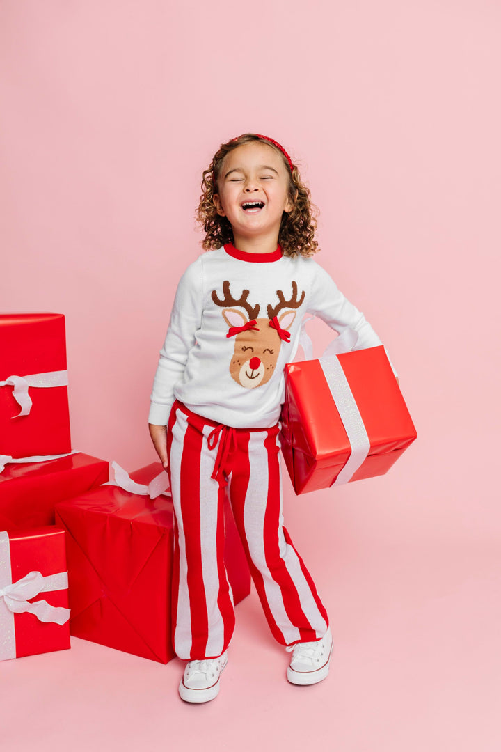 little girl holding Christmas gift in white sweater with Rudolph wearing 3D pigtail bows paired with red and white cotton knit sweater pants