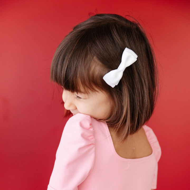 little girl in pink twirl dress and white satin pigtail bows