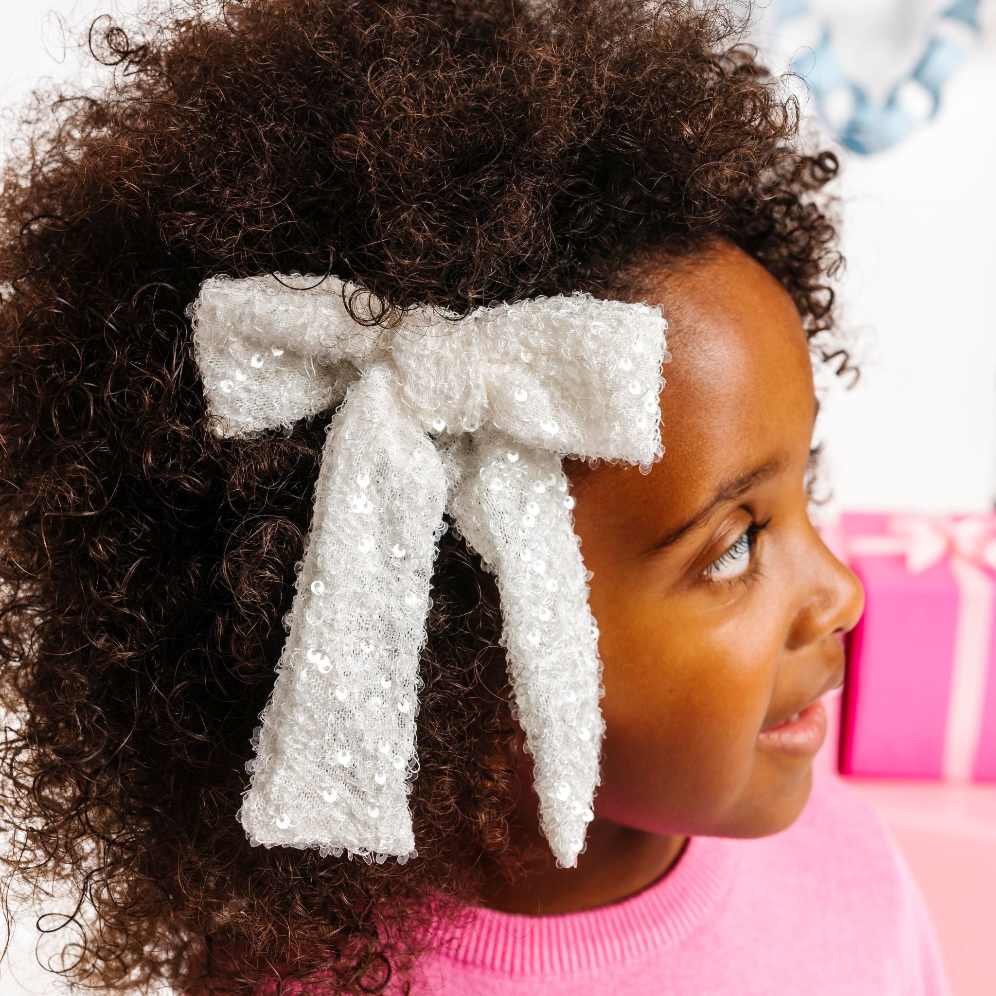 little girl in fuzzy white sequin bow on clip paired with pink Christmas sweater for winter wonderland vibes