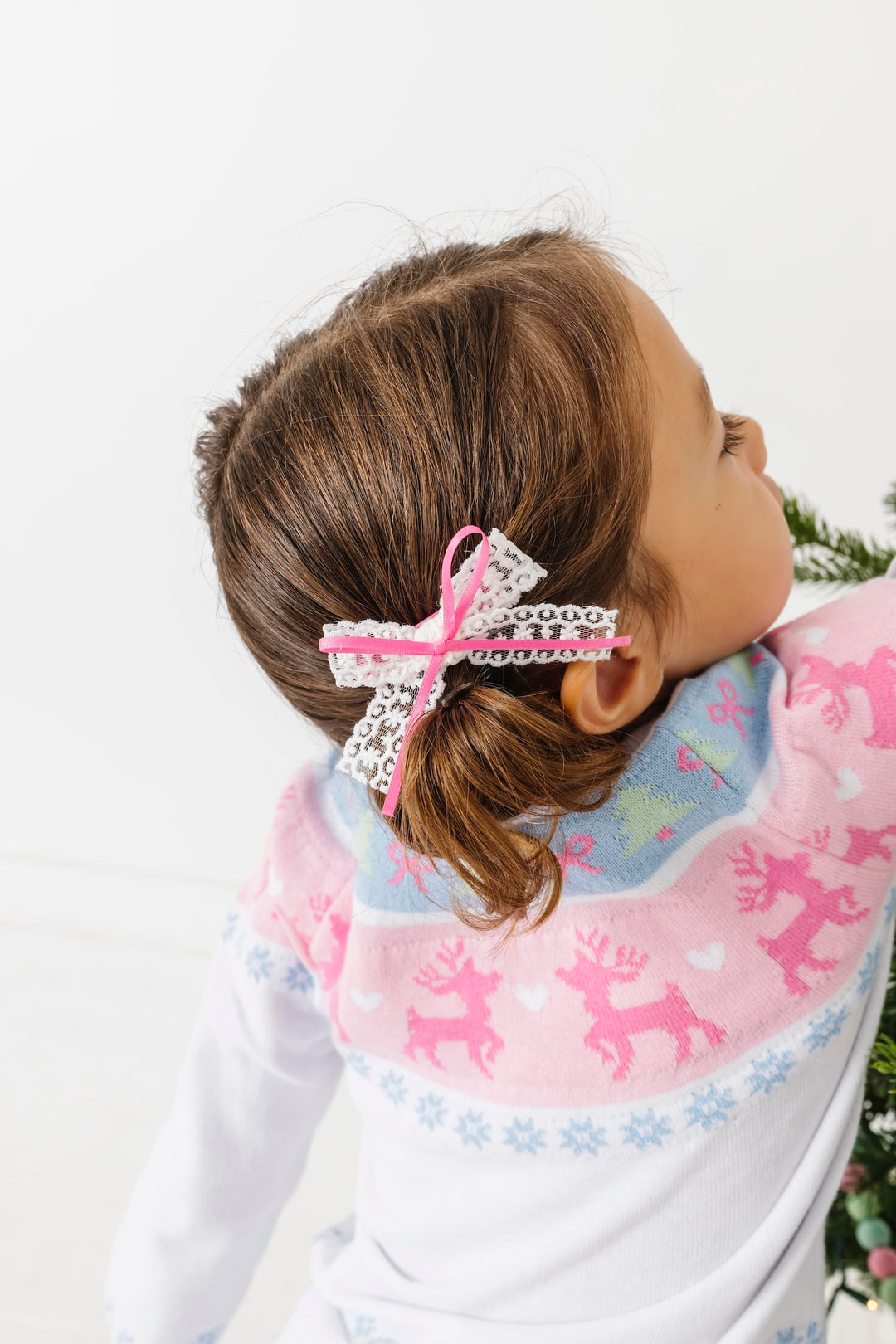little girl in pastel christmas fair isle sweater with matching white lace pigtail bows with pink satin ribbon tied on top