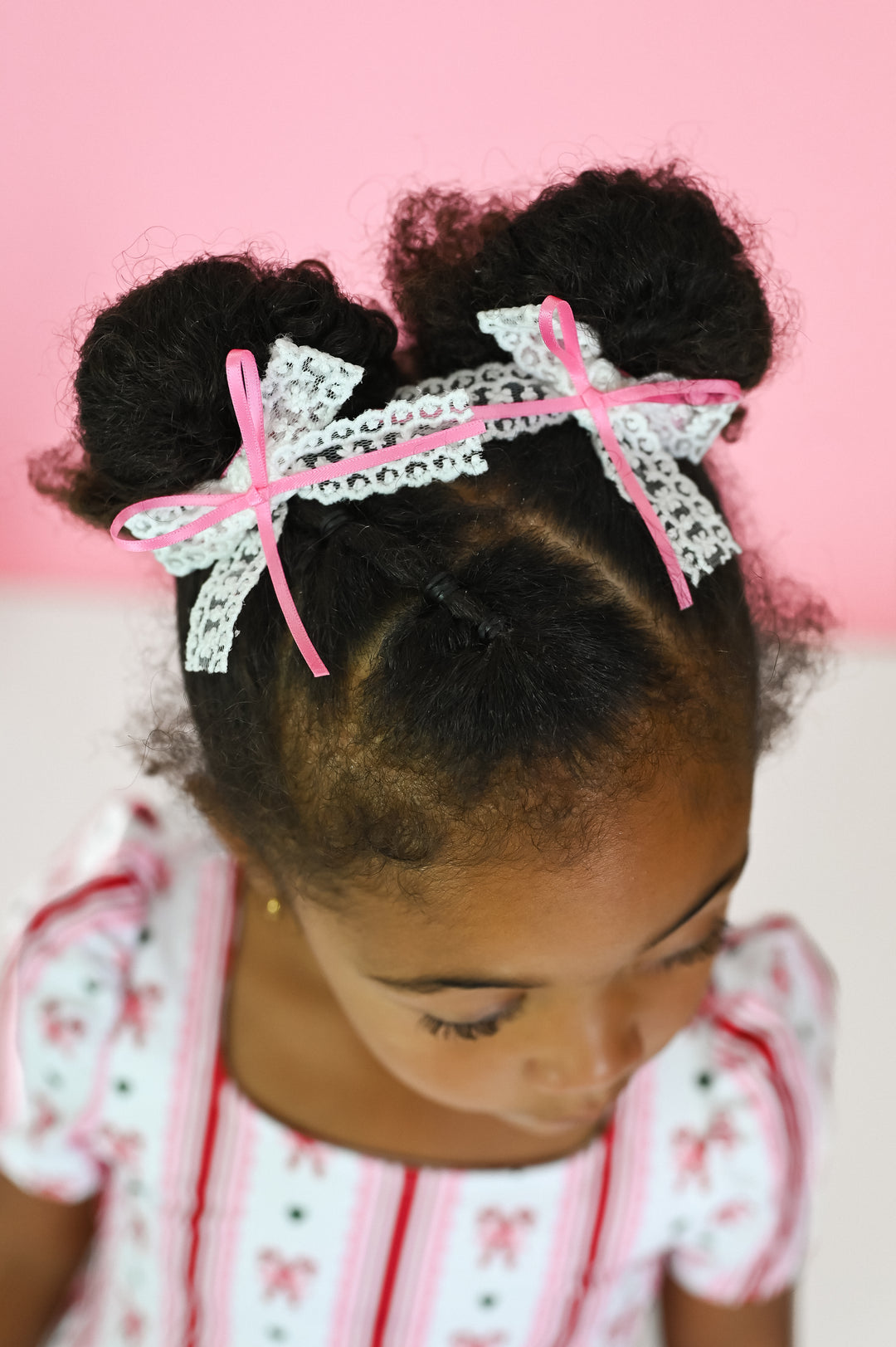 little girl in candy cane print dress with matching white lace pigtail bows with pink satin ribbon tied on top