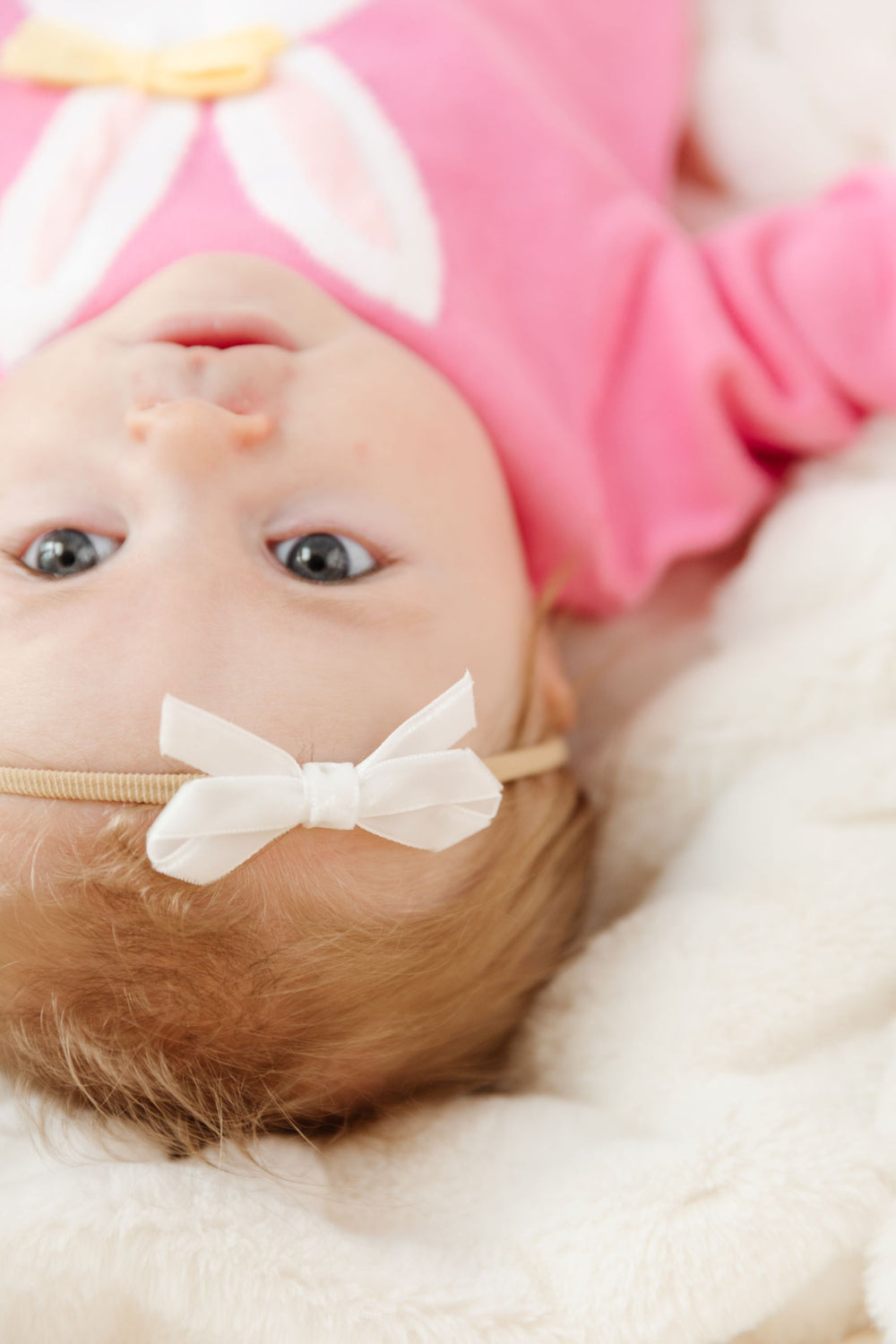 closeup of baby girl wearing white velvet ribbon bow on stretchy nylon headband to match pink easter bunny sweater set