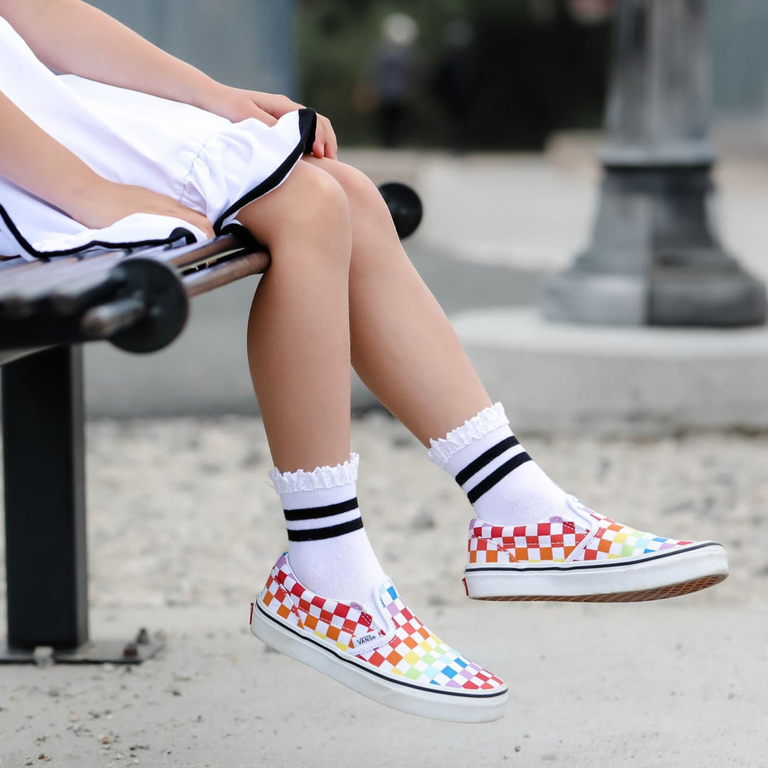 little girl sitting on bench wearing checkered vans and white and black striped lace midi socks