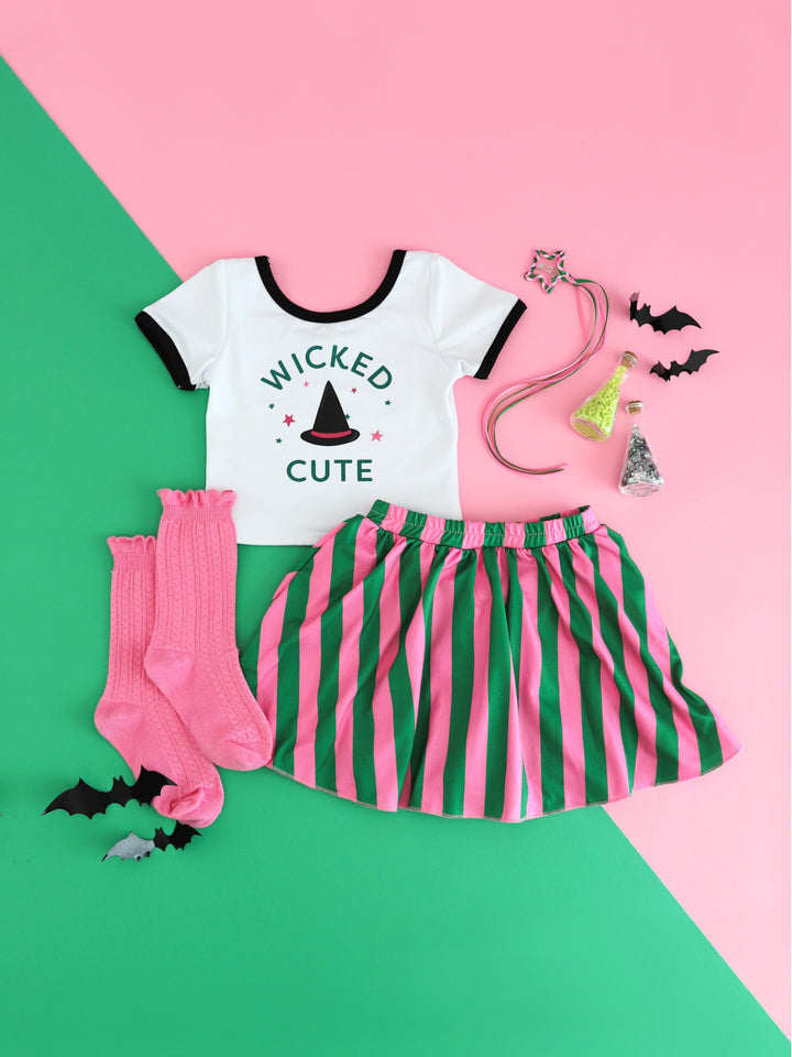 girls' Wicked inspired outfit with fitted white top featuring "wicked cute" design with witch hat, green and pink striped skort, pink knee highs and matching star ribbon clip