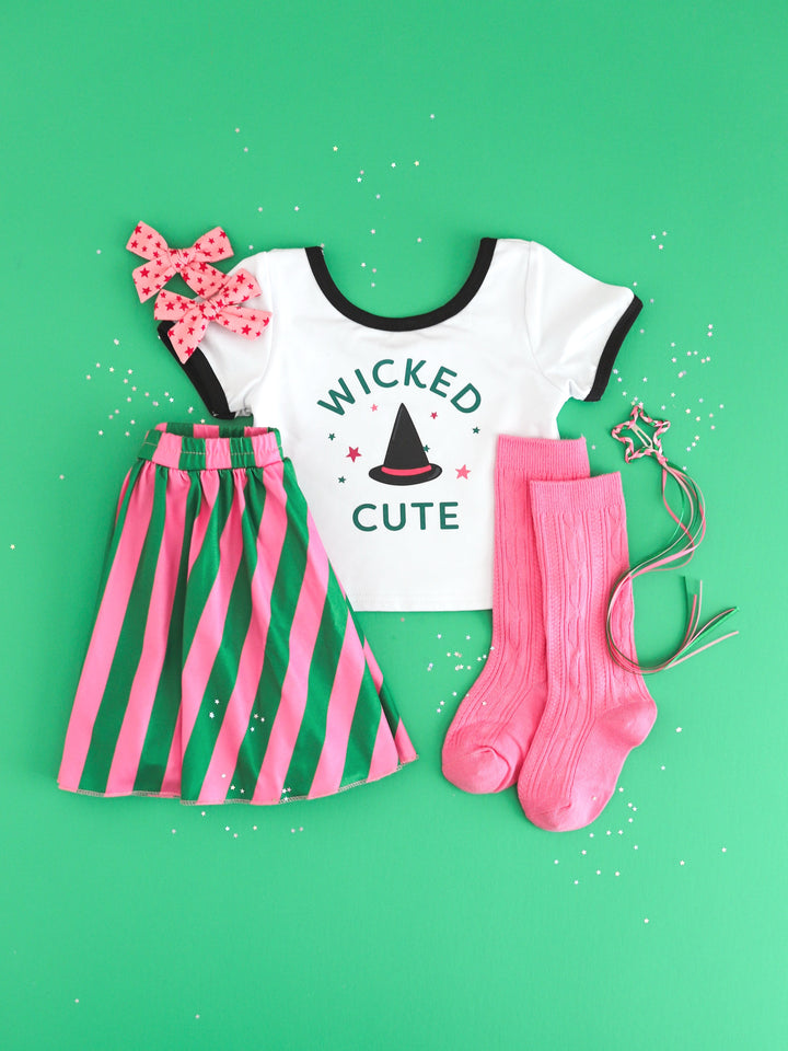 styled flatlay for girls' fitted tee with "Wicked Cute" design paired with pink and green striped skort, pink knee highs and pink star pigftail bows