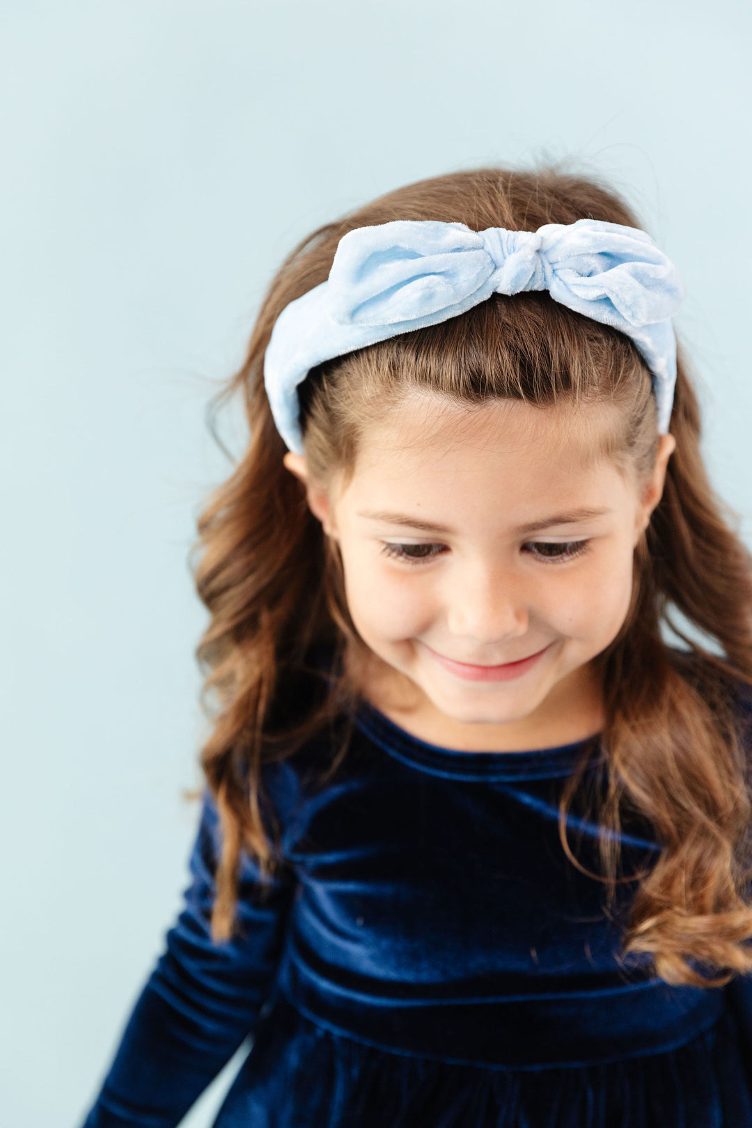 little girl wearing light blue velvet headband with dark blue velvet dress