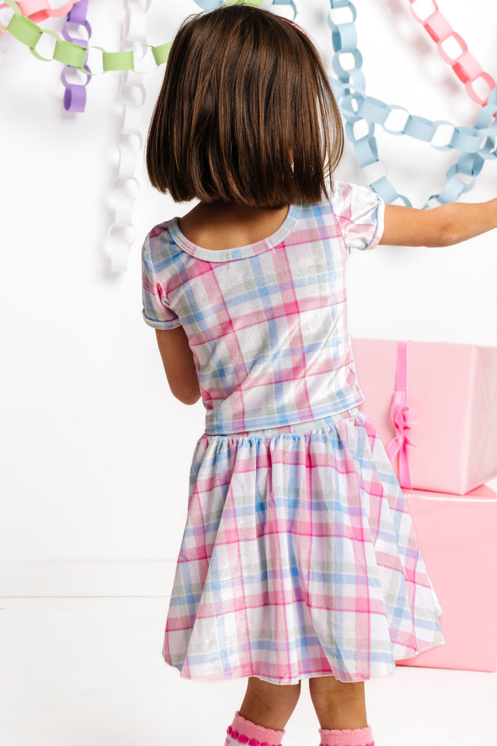 back view of little girl in scoop back fitted velvet top in white, pink, blue and green plaid paired with matching skirt