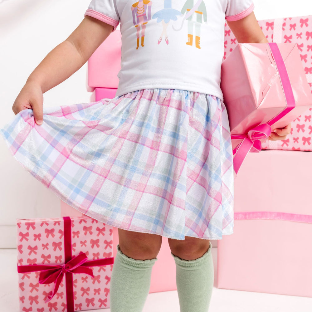 little girl holding pink Christmas gift in pastel velvet plaid shirt to match nutcracker top