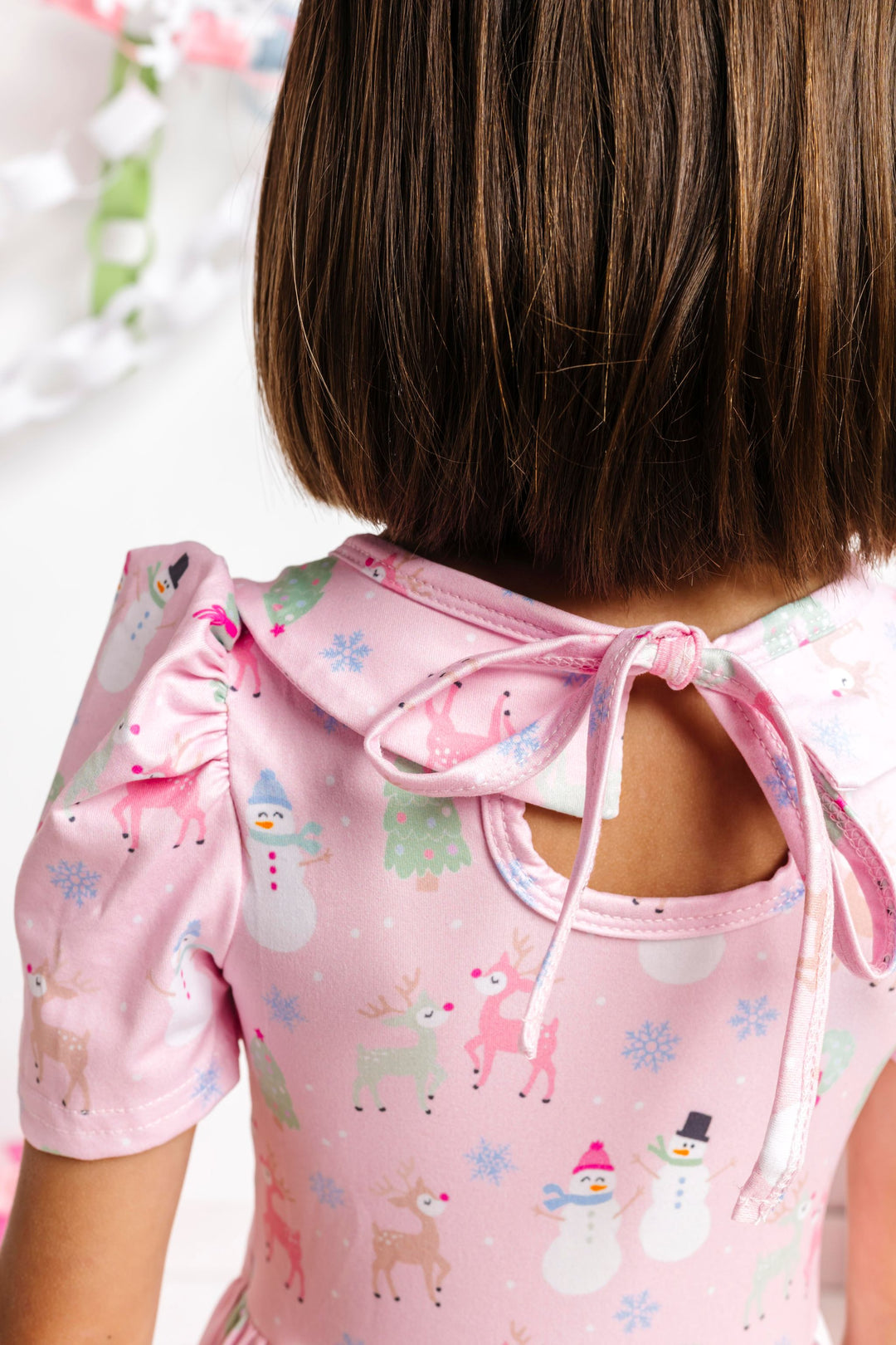 closeup of little girl in tie back collared puff sleeve twirl dress in light pink with pastel winter themed print
