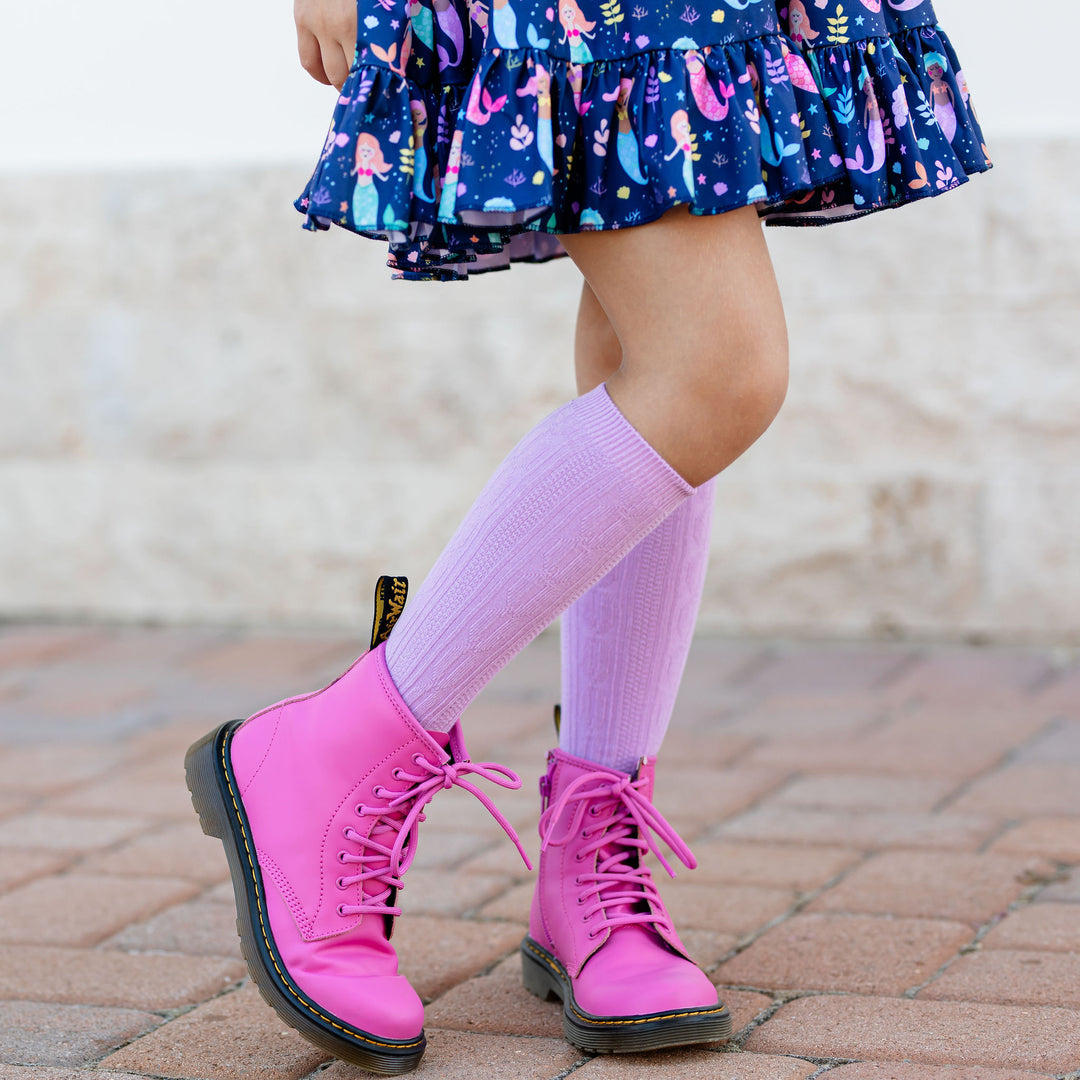 little girl wearing light purple cable knit knee socks and bright pink boots