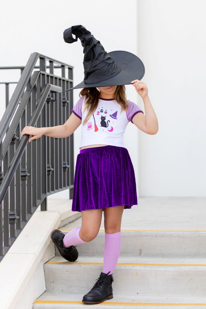 little girl in witch hat with witchy themed fitted top, purple velvet skort and light purple knee highs