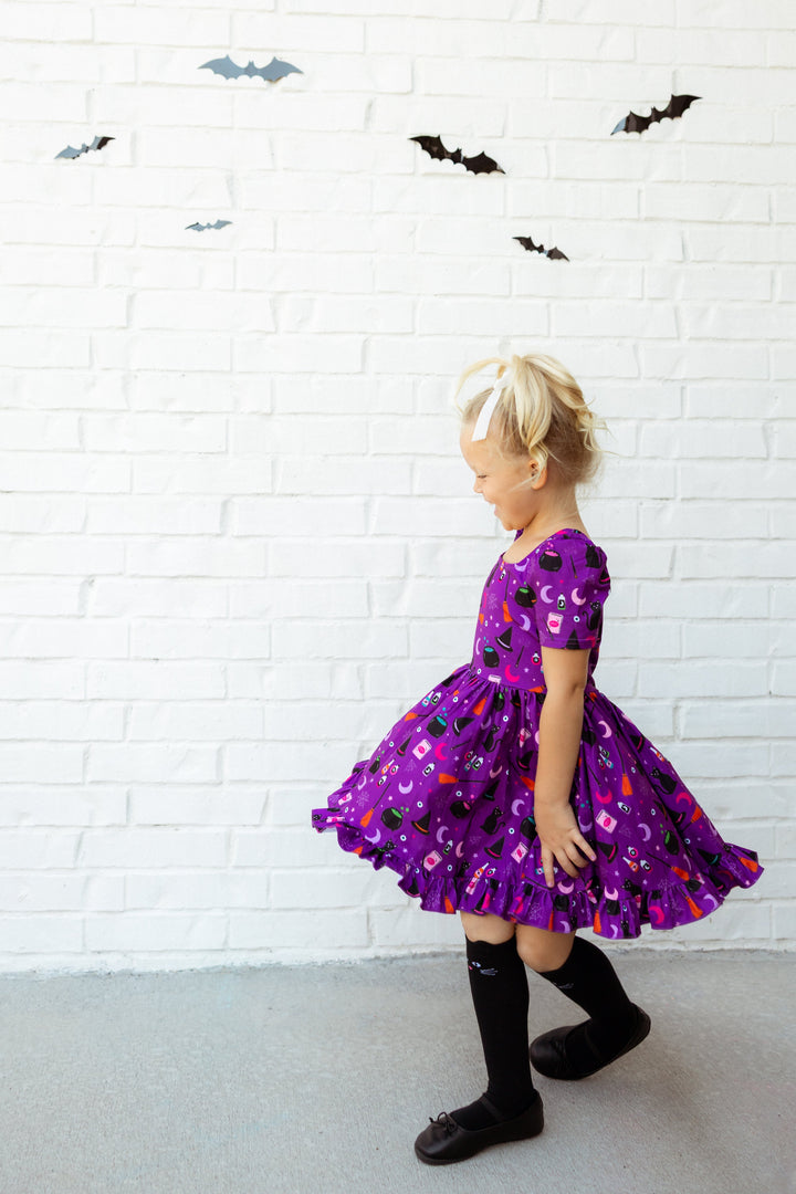little girl twirling in purple witch themed dress with black cat knee highs socks and bats in the background
