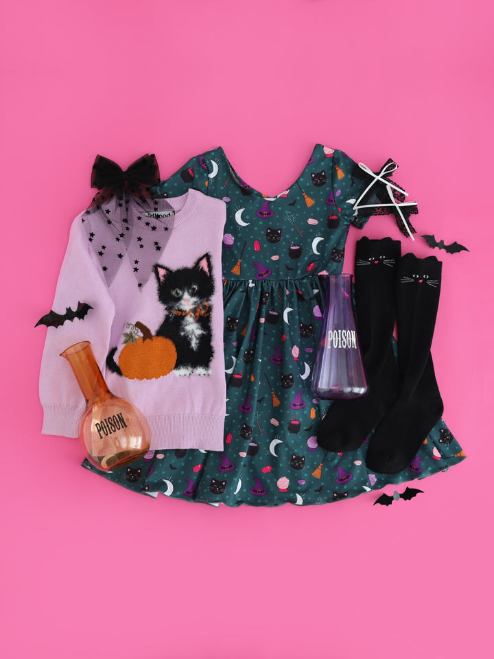 flat lay photo on bright pink featuring teal witch print twirl dress, lavender cotton knit sweater with fluffy black cat and sparkly pumpkin design, black cat knee socks and coordinating hair bows