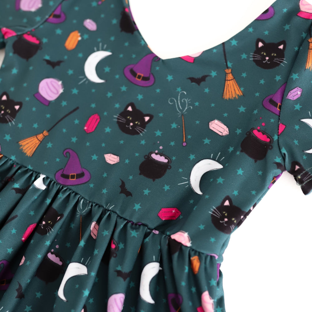 closeup of girls' teal witch themed Halloween twirl dress print with stars, black cats, witch hats and cauldrons