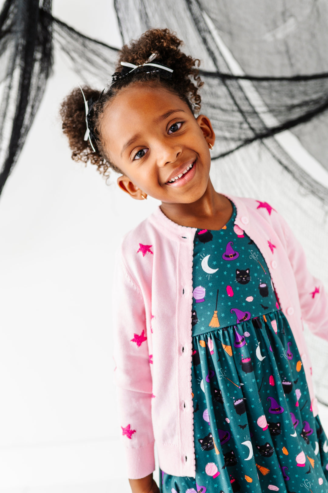 young girl in team witchy print twirl dress paired with light pink cotton knit cardigan with hot pink sparkly star design