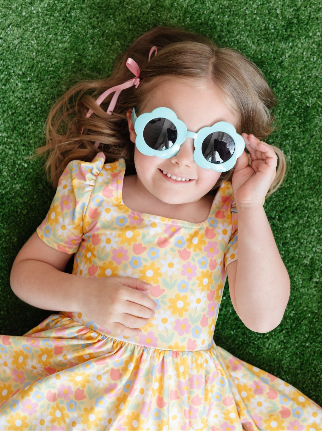 Girl in summer square neck twirl dress with summer yellow floral print laying on grass looking up in sunglasses