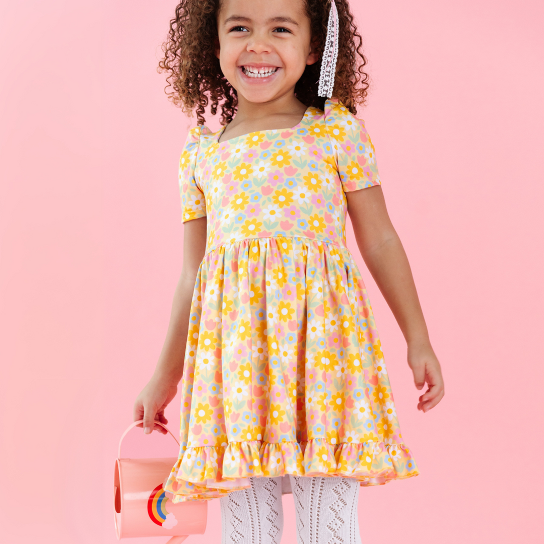 little girl holding watering can in yellow spring floral twirl dress with white pointelle knit tights