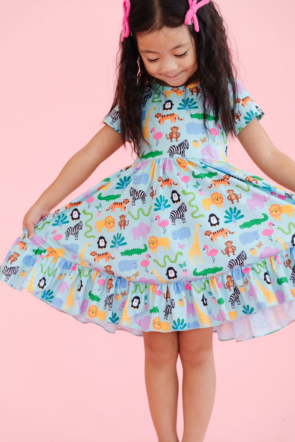 girl wearing short sleeve, ruffle hem twirl dress in mint with colorful zoo animal print and matching pink bows