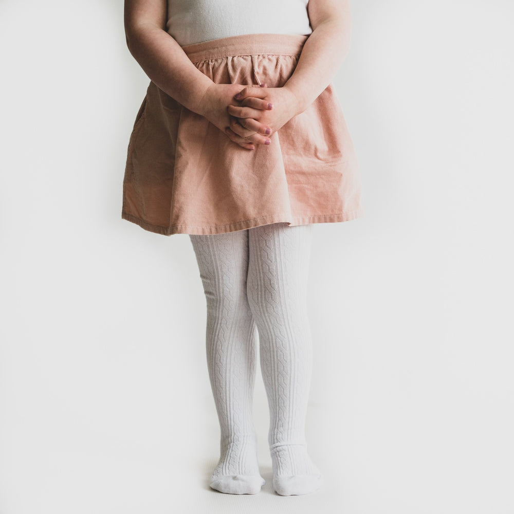 White cable knit tights on little girl with pink skirt.