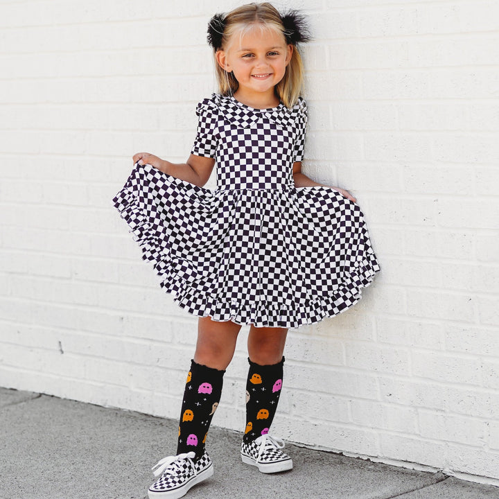 little girl in black and white checkered twirl dress and cute ghost socks