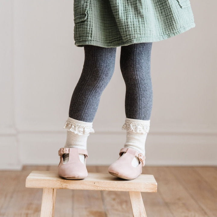 little girl on stool wearing charcoal grey tights with lace midi socks and blush pink t-strap shoes