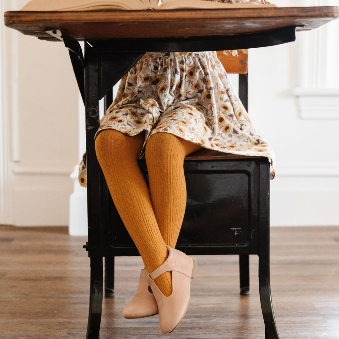 little girl at vintage school desk wearing mustard cable knit tights