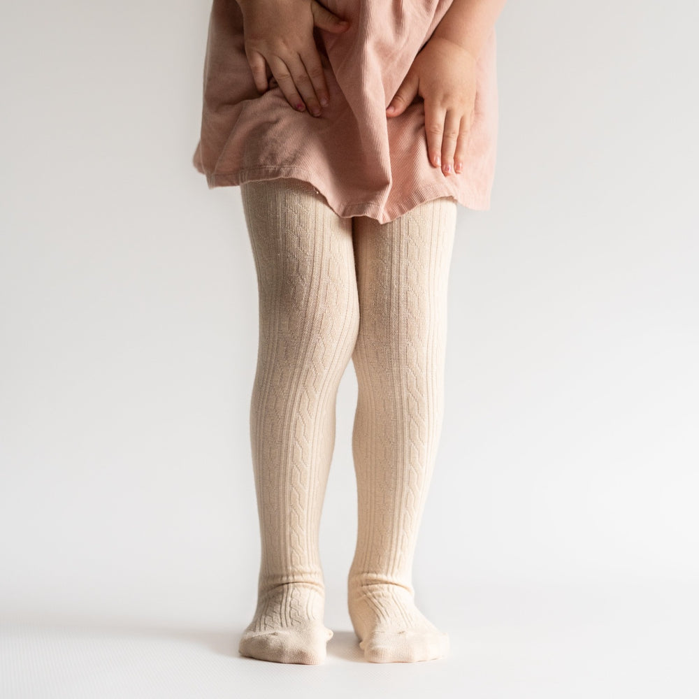 Cream cable knit tights on little girl with pink skirt.